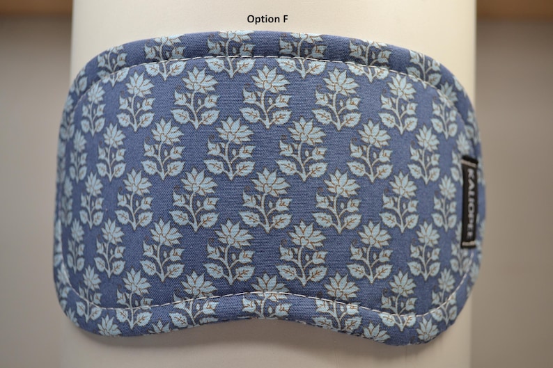 K&ouml;nnte beinhalten: Eine blaue Augenmaske mit einem Blumenmuster in Hellblau und Braun. Die Maske hat eine gebogene Form und ist an den R&auml;ndern gen&auml;ht. Der Text "Option F" steht oben.