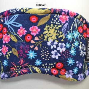 K&ouml;nnte beinhalten: Eine marineblaue Schlafmaske mit einem farbenfrohen Blumenmuster. Das Design zeigt rosa, rote, gelbe und blaue Blumen und Bl&auml;tter. Die Maske hat einen gen&auml;hten Rand und ein kleines schwarzes Etikett mit der Aufschrift "KALIOPEE".