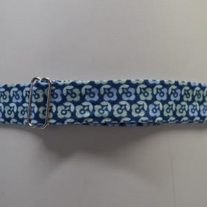 K&ouml;nnte beinhalten: Ein blauer Stoffhalsband mit einem sich wiederholenden Blumenmuster in Hellblau und Gr&uuml;n. Eine silberfarbene Metallschnalle ist am Halsband befestigt. Das Halsband ist f&uuml;r ein Haustier bestimmt.