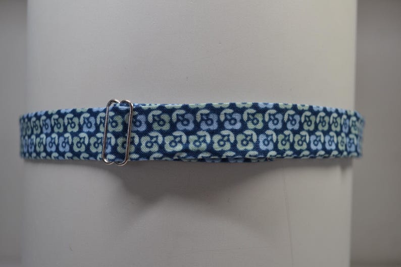 K&ouml;nnte beinhalten: Ein blauer Stoffhalsband mit einem sich wiederholenden Blumenmuster in Hellblau und Gr&uuml;n. Eine silberfarbene Metallschnalle ist am Halsband befestigt. Das Halsband ist f&uuml;r ein Haustier bestimmt.