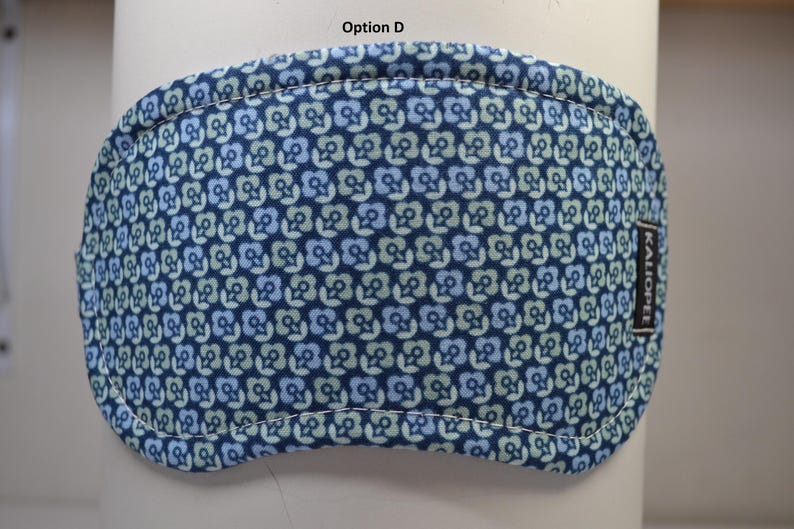 K&ouml;nnte beinhalten: Eine blaue Augenmaske mit einem Blumenmuster in Blau- und Gr&uuml;nt&ouml;nen. Die Maske hat einen wei&szlig; gen&auml;hten Rand und ein kleines schwarzes Etikett mit wei&szlig;em Text, auf dem "KALIOPEL" steht. Der Text "Option D" steht oben.