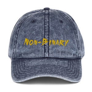 May include: A blue denim vintage style baseball cap with the words "NON-BINARY" embroidered in yellow.