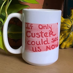 Könnte beinhalten: Eine weiße Keramiktasse mit einer roten und weißen Grafik, auf der "If Only Custer Could See Us Now" steht.