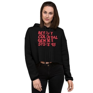 Puede incluir: Sudadera negra con capucha corta con un gráfico rojo que dice "Betray Colonial Gender Systems".