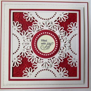 May include: A white card with a red background and a white lacy design. The center of the card has a circle with the text "Filled with joy".