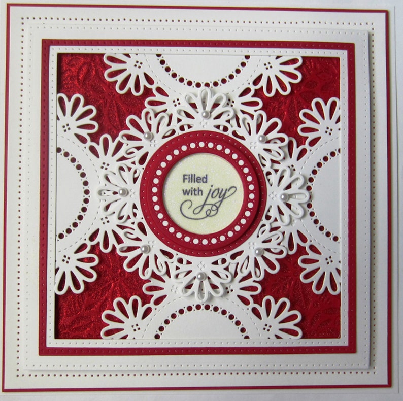 May include: A white card with a red background and a white lacy design. The center of the card has a circle with the text "Filled with joy".