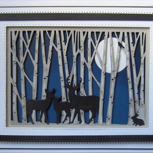 May include: A paper craft scene depicting a moonlit forest with a full moon, a flock of birds flying overhead, and a family of deer standing in the foreground. The forest is made of white paper with a blue background.