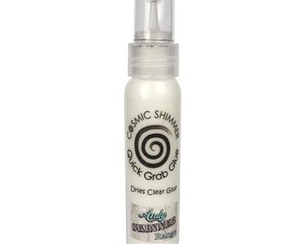 Puede incluir: Una botella blanca de pegamento Cosmic Shimmer Quick Grab Glue. La botella tiene una tapa transparente y una etiqueta que dice "Cosmic Shimmer Quick Grab Glue" y "Dries Clear Glue". La etiqueta también tiene un diseño de espiral y el texto "Andy Skinner Range".