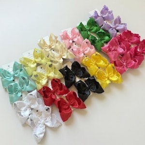 May include: A collection of colorful hair bows in various shades, including white, red, black, yellow, pink, green, and purple. Each bow is neatly arranged on a white card, showcasing the variety of colors and styles available.