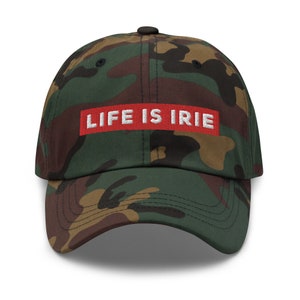 May include: Camouflage baseball cap with the text "LIFE IS IRIE" in white letters on a red rectangle. The cap features a curved brim and a black button on top.