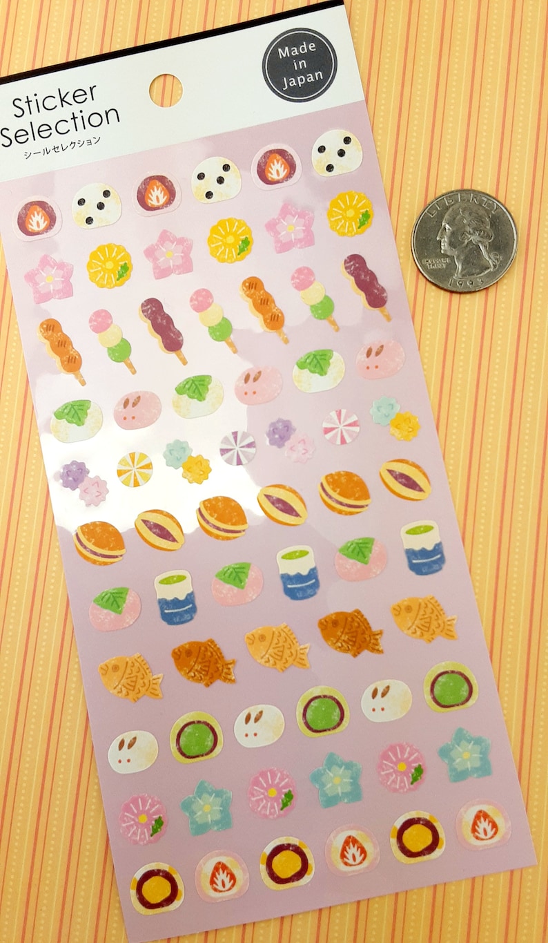 May include: A sheet of stickers featuring various Japanese food and cultural icons. The stickers are on a light purple background and include images of dango, mochi, taiyaki, and flowers. The sheet is labeled "Sticker Selection" in Japanese and English. The sheet also includes the text "Made in Japan".