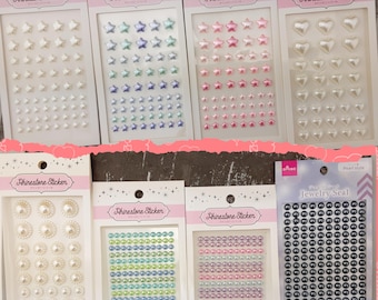 May include: Assortment of rhinestone stickers in various colours and shapes, including stars, hearts, and circles. The stickers are packaged on individual cards with the text "Rhinestone Sticker" printed on each card.
