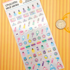 May include: A sheet of colorful stickers featuring various beauty and makeup themed illustrations. The stickers include nail polish bottles, makeup palettes, lipstick tubes, perfume bottles, hairbrushes, mirrors, and a vanity set. The sheet is labeled "chocotto seal series" and includes the text "When we feel life's warmth, it's a sure proof that we are alive."