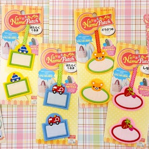 May include: Assortment of colorful iron-on name patches and stickers for clothing. The patches feature various themes, including cars, animals, and sweets. The text on the patches reads "Name Patch" and "Wappen".