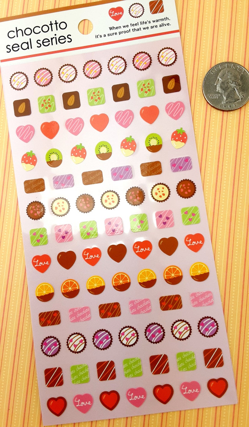 May include: A sheet of pink and white stickers featuring various chocolate-themed designs. The stickers include hearts, squares, circles, and other shapes with different chocolate fillings, such as almonds, strawberries, kiwi, and orange slices. The text "chocotto seal series" and "Love" appears on the sheet.