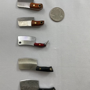 May include: Five miniature cleavers with wooden and black handles. The cleavers are arranged vertically, with the smallest at the top and the largest at the bottom. A US quarter is included for scale.