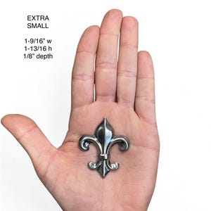 May include: A small, silver-colored fleur-de-lis emblem. The emblem is 1-9/16 inches wide, 1-13/16 inches high, and 1/8 inch deep. The text "EXTRA SMALL" is above the measurements.