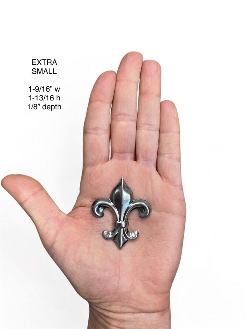 May include: A small, silver-colored fleur-de-lis emblem. The emblem is 1-9/16 inches wide, 1-13/16 inches high, and 1/8 inch deep. The text "EXTRA SMALL" is above the measurements.