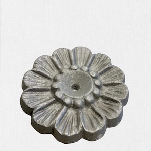 Puede incluir: Una pieza decorativa de metal plateado con forma de flor y un pequeño agujero en el centro.