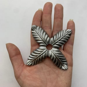 May include: A silver metal decorative piece with a four-leaf clover design. The piece has a hole in the center.