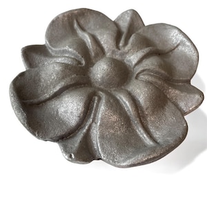 May include: A silver metal flower-shaped decorative piece with a raised centre and five petals.