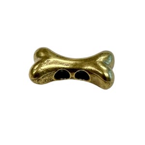 May include: A gold-coloured metal dog bone charm with two holes for attaching to a necklace or bracelet.