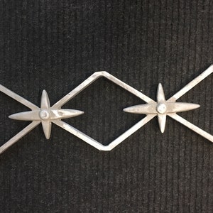 May include: A silver metal decorative piece with two star-shaped designs and a diamond shape in the centre.