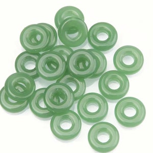 May include: A collection of 18 light green jade donut beads. The beads are smooth and have a hole in the center.
