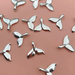 May include: A collection of silver-toned whale tail charms. The charms are shaped like a whale's tail and have a hole at the top for attaching to jewelry or other crafts.