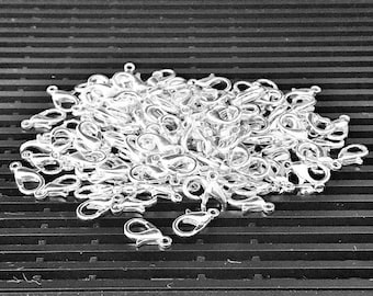 Op de afbeelding: Een grote stapel zilverkleurige karabijnhaken. De karabijnhaken zijn een populaire toevoeging voor het maken van sieraden.