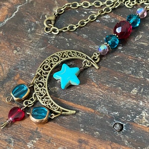 May include: A gold crescent moon charm necklace with a turquoise star charm and blue and red glass beads.