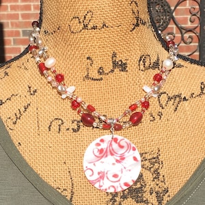 May include: A red and white shell pendant necklace with a red and white swirl design. The necklace is made with red and white beads and silver beads.