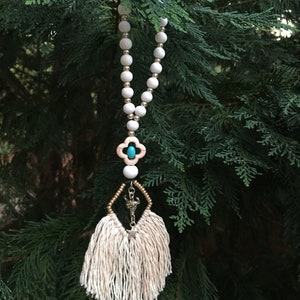 May include: A white beaded necklace with a turquoise and gold charm and a white tassel hanging from it.