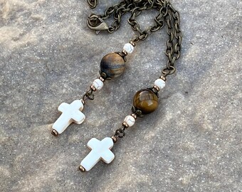 May include: A long necklace with a brown chain, white beads, and two tiger's eye beads. The necklace has two white cross charms.
