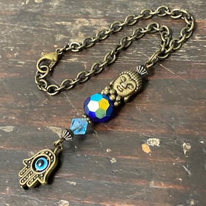 May include: A gold chain with a blue and green crystal bead, a gold Buddha charm, and a gold hamsa hand charm with a blue evil eye.