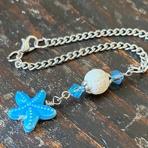 May include: A silver chain bracelet with a blue starfish charm, a white lava bead, and blue crystal beads.