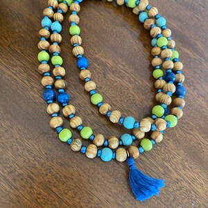 May include: A wooden beaded necklace with green, blue, and brown beads. The necklace has a blue tassel at the end.
