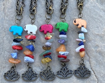 May include: Five necklaces with a lotus charm and a stack of colorful gemstone beads. Each necklace features a different colored elephant charm: blue, white, pink, green, and orange.