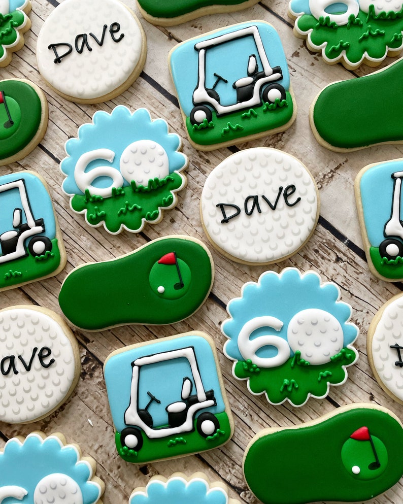 May include: A set of 10 golf-themed sugar cookies decorated with blue, green, and white icing. The cookies feature golf balls, golf carts, and the number 60. Some cookies also have the name "Dave" written on them.