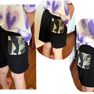 May include: Black shorts with a large, colorful pocket on the back. The pocket has a graphic design of a person with a hat and a flower.