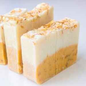 Puede incluir: Tres barras rectangulares de jab&oacute;n artesanal. La mitad superior de cada barra es blanca, pasando a un tono amarillo-naranja en la parte inferior. La parte superior de cada barra est&aacute; salpicada de peque&ntilde;os copos de color marr&oacute;n claro. Los jabones est&aacute;n dispuestos sobre una superficie blanca.