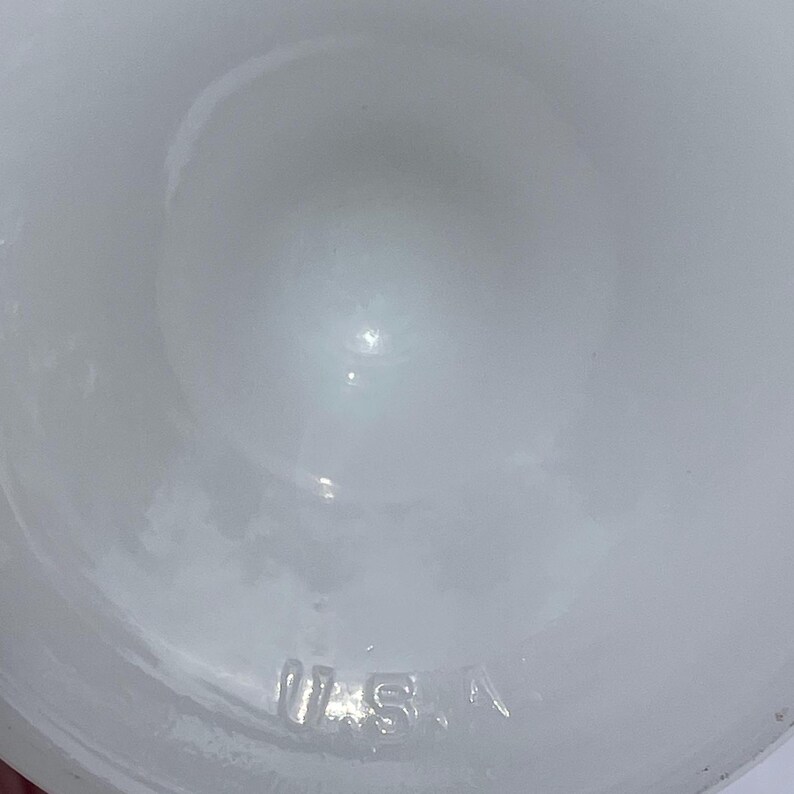 May include: A white, opaque glass object with a rounded shape. The letters "U.S.A." are embossed on the bottom of the object. The object has a smooth, glossy surface.