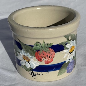 May include: A small, white ceramic crock with blue stripes and hand-painted flowers and strawberries. The crock is signed "Hazel" on the bottom.