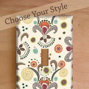 Puede incluir: Tres tapas para interruptores y enchufes con un patrón abstracto colorido. Las tapas están etiquetadas como "Standard Cover", "Decora/Rocker Cover" y "Outlet Cover".