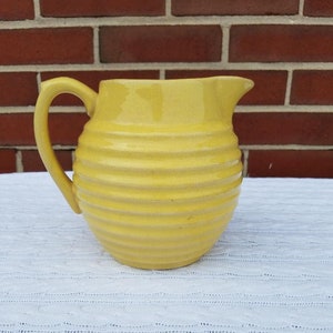 May include: A yellow ceramic pitcher with a ribbed design. The pitcher has a handle and a spout.