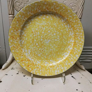 May include: A yellow and white enamel dinner plate with a black rim. The plate has a speckled pattern.