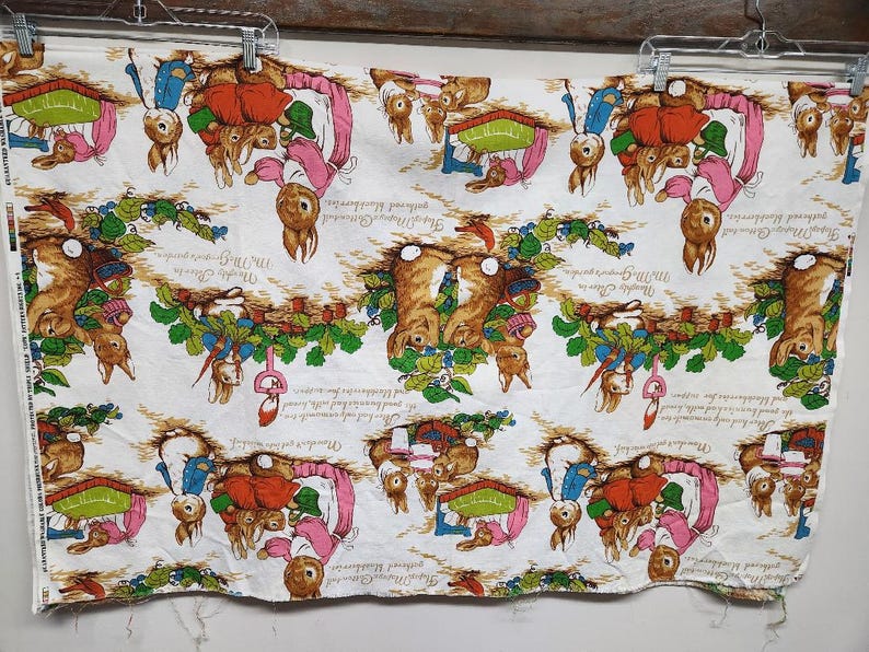 May include: White fabric with a repeating pattern of Peter Rabbit characters. The fabric features Peter Rabbit and his friends in various scenes, including gardening, playing, and enjoying the outdoors. The fabric is printed with the text "The Tale of Peter Rabbit" and "Beatrix Potter".