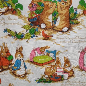 May include: A white fabric with a repeating pattern of bunnies and blueberries. The bunnies are brown and white with pink noses. The blueberries are blue and green. The fabric has the text "The Tale of Peter Rabbit" printed on it.