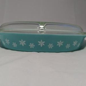 May include: A turquoise blue glass baking dish with a clear glass lid. The dish has a white snowflake pattern around the rim.