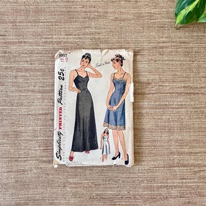 May include: Vintage Simplicity printed sewing pattern 1997, size 14, bust 32. The pattern features illustrations of two slip dresses. The cover is off-white with black text and illustrations. The dress on the left is a long, dark dress, and the dress on the right is a blue dress.